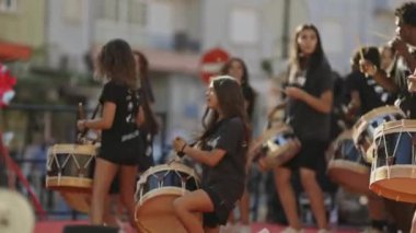 5 Temmuz 2024, Almada, Portekiz - geçit töreninde davul çalan bir grup genç kadın. Davulcular siyah gömlek giyiyorlar ve çeşitli davullar çalıyorlar. Manzara enerjik ve canlı.