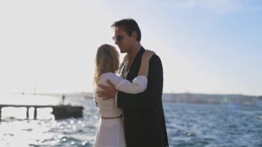 Gün batımında okyanusun kenarında yavaş dans eden bir kadın ve erkek kucaklaşıyorlar. Batan güneşin gölgesinde kalmışlar..