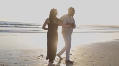 Bir adam ve bir kadın sahilde dans ediyorlar. Adam beyaz bir gömlek giyiyor ve kadın siyah bir elbise giyiyor. Sahne romantik ve eğlenceli.