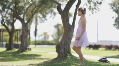 Açık renk elbiseli bir kadın güneşli bir günde parkta dans eder..