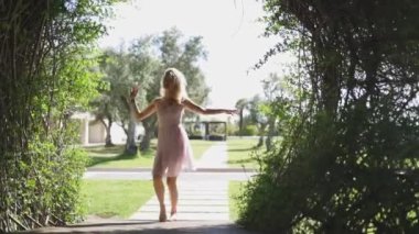 Pembe elbiseli bir kadın parkta asfalt bir yolda dans ediyor. Gülümsüyor ve güzel havanın tadını çıkarıyor..