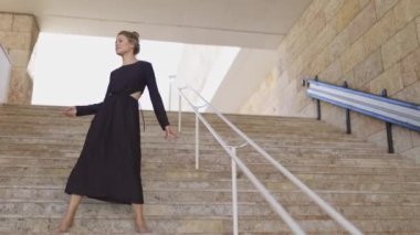 Siyah elbiseli bir kadın merdivenlerden yukarı çıkıyor. Zarafet ve entelektüellik kavramı. Kadın şık giyinmiş ve adam kendine güvenerek yürüyor.