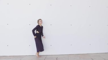 Mor elbiseli bir kadın beyaz bir duvarın önünde dans ediyor. Özgürlük ve ifade kavramı, kadın kollarını ve bacaklarını akışkan bir hareketle hareket ettiriyor.