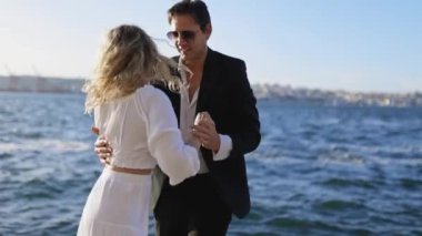 Gün batımında okyanusta dans eden bir çiftin romantik videosu. Güneş arka planda batıyor, sıcak ve romantik bir atmosfer yaratıyor. Çift batan güneşe karşı siluetlendi..