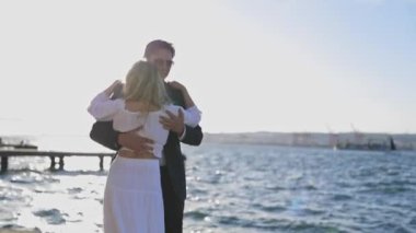 Gün batımında okyanusun kenarında yavaş dans eden bir kadın ve erkek kucaklaşıyorlar. Batan güneşin gölgesinde kalmışlar..