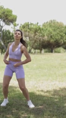 Mor bluzlu ve şortlu bir kadın parkta dikey dans ediyor.