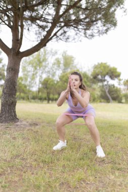 Atletik giyinen genç bir kadın parkta direniş bandı çalıyor. Spor yaparken yüzüne odaklanıyor..