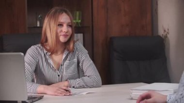 İş görüşmesi. Masada oturan bir kadının arkasında bir adam duruyor. Adam kadına bakıyor ve onun dikkatini çekmeye çalışıyor.