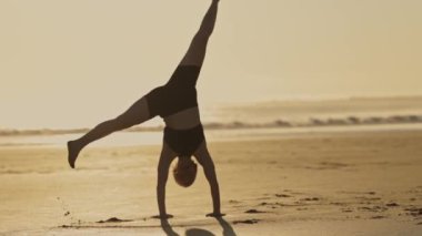 Bir kadın plajda akrobatik egzersizler yapıyor. Okyanus kenarında gün batımı.