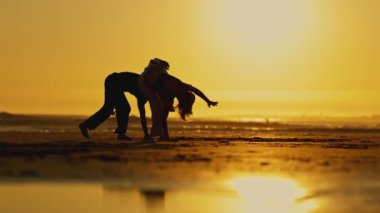 Bir kadın ve erkek silueti - sportif çift gün batımında okyanus kenarında dövüş eğitimi yapıyorlar - yavaş çekim
