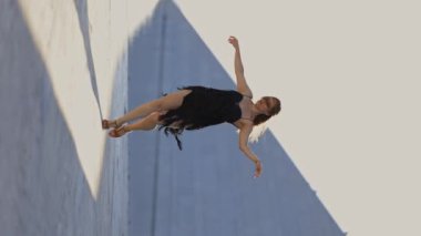 Siyah elbiseli bir kadın havada dans figürü yapıyor. Kadın yer çekimine meydan okuduğu için görüntüde özgürlük ve hareket duygusu var.