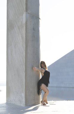 Dansçı, çatıdaki beton sütunlara dokunurken zarifçe poz verir.