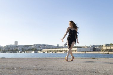 Genç bir kadın, arka planda şehir olan bir iskelede Latin dansı yapıyor.