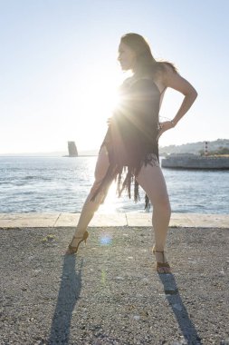 Profesyonel dansçı denizin önünde klasik bir latin dans kıyafeti içinde poz veriyor.