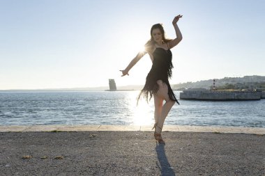 Genç kadın gün batımında rıhtımda Latin dansı yapıyor.