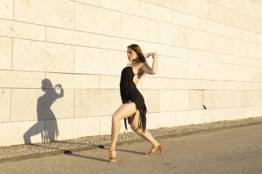 Genç bir kadın güneşli bir günde duvarın önünde Latin dansı yapıyor.