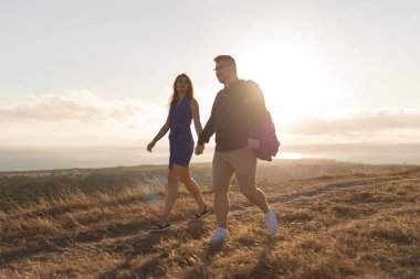 Genç çift gün batımında bir tepede yürürken romantik bir anın tadını çıkarıyor.