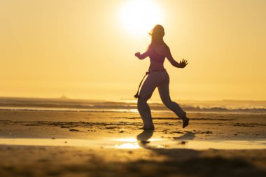 Gün batımında sahilde Capoeira çalışan bir kadının silueti, o anın huzuru ve sessizliğinin tadını çıkarıyor.