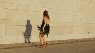 Siyah elbiseli kadın duvarın önünde dans ediyor, gölgesi yerde.