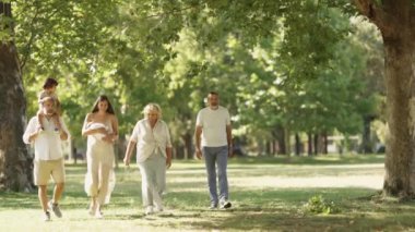 Aralarında bir bebek, anne-baba ve büyükbaba 'nın da bulunduğu çok nesilli aile, yemyeşil bir parkta sakin bir gezintinin tadını çıkarıyor.