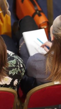 Kadın dikkatle bir konferans konuşmasını dinlerken not defterine notlar alıyor.