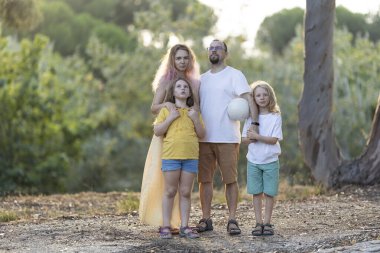 Dört kişilik aile, voleybol oynarken parkta birlikte poz veriyorlar.