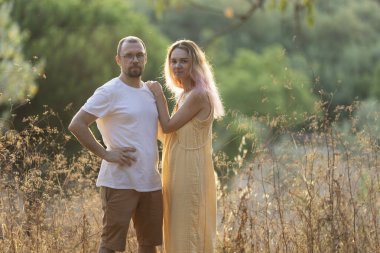 Bir adam ve bir kadın altın saatinde bir tarlada poz veriyorlar.