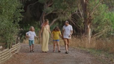 Dört kişilik aile, doğanın güzelliğiyle çevrili huzurlu bir toprak yolda sakin bir gezinti yapıyor.