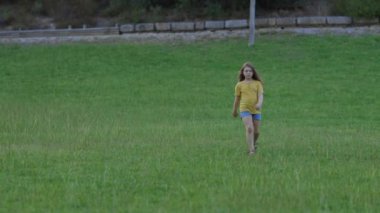 Genç kız güneşli kır çiçekleri tarlasında zarifçe yürüyor