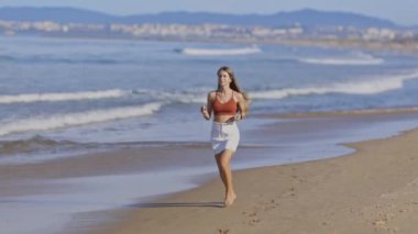Genç kadın kumlu sahil şeridinde neşeyle koşuyor.