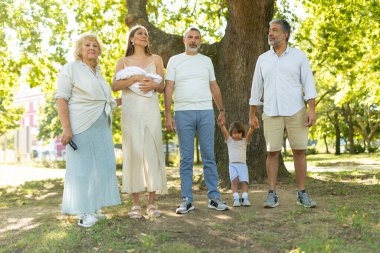 Mutlu aile parkta yan yana dururken fotoğraf çektirmek için poz veriyor.