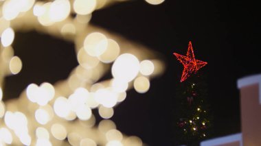 Noel ağacının tepesinde parlayan bir yıldız ve arka planda bulanık ışıklar