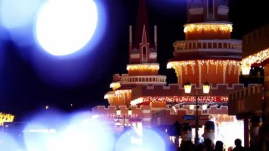 İnsanlar geceleri ışıklarla kaplı tuhaf bir binanın önünden geçen bir şehirde yürüyorlar.