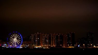 Dönme dolap geceleri renk değiştiriyor. Arka plandaki bir şehrin binalarını aydınlatıyor.