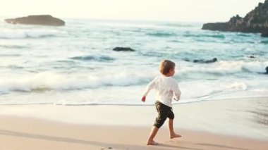 Genç çocuk sevinçle sahilde koşuyor, ayaklarının altındaki kumu ve okyanus esintisini hissediyor.