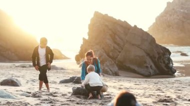 Güneşli bir plajda kumdan kaleler inşa ederken birlikte oynayan neşeli bir aile.