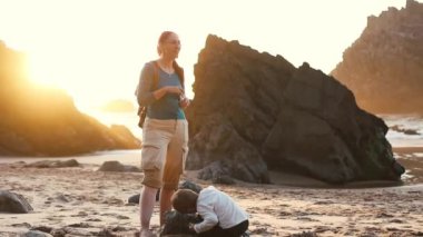 Anne ve oğlu gün batımında kumlu bir plajda güzel vakit geçiriyorlar.