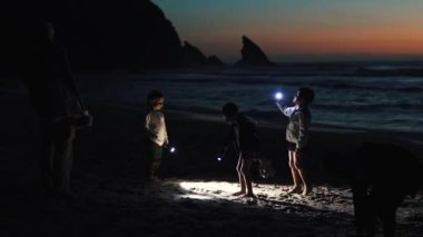 Çocuklar gün batımında plajda el fenerleriyle oynarken eğleniyorlar.