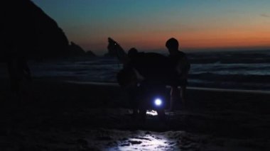 Siluetli çocuklar gün batımından sonra plajda fenerlerle koşup oynuyorlar.