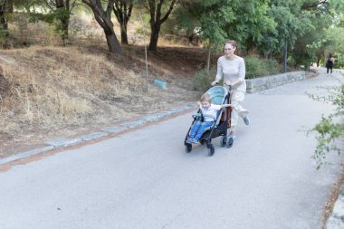 İçinde çocuk olan bir bebek arabasını iten bir kadın. Çocuk gülümsüyor ve kadın da gülümsüyor. Sahne huzurlu ve mutlu.