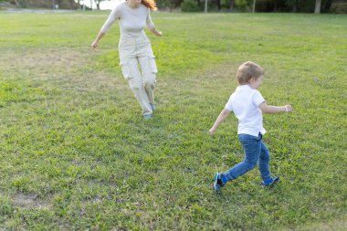Anne ve oğlu güneşli bir günde parkta koşuyorlar.