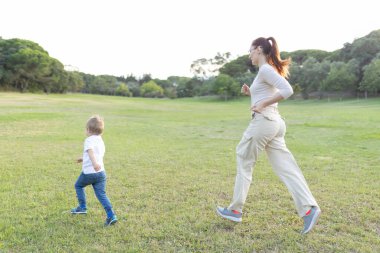 Anne ve oğlu güneşli bir günde parkta birlikte koşuyorlar.