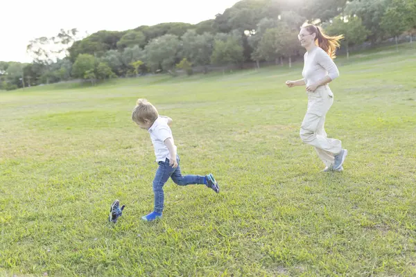 Anne ve oğlu çimenli bir parkta koşup oynuyorlar.