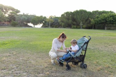 Anne, parkta güzel bir günün tadını çıkarırken bebek arabasının emniyet kemerini bağlıyor.