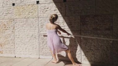 Balerin nezaketle bale rutinini uyguluyor, destek ve denge için korkuluk kullanıyor.