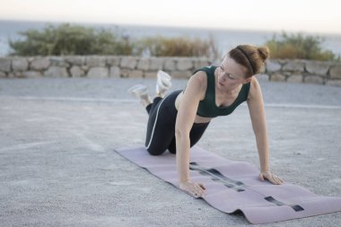 Kadın deniz kenarındaki spor minderinde şınav çekiyor.