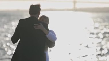 Bir erkek ve bir kadın gün batımında suyun kenarında dans ediyorlar.