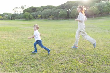 Anne ve oğlu parkta birlikte koşmaktan zevk alıyorlar.