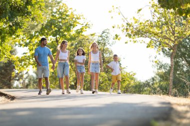 Aile, ağaçlık bir yolda birlikte yürümekten zevk alıyor.
