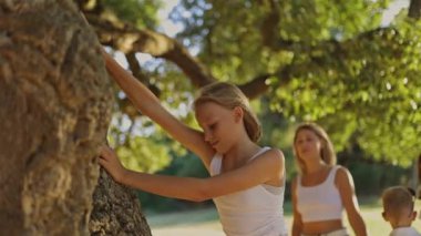 Mutlu bir aile parkta eğleniyor, güneşli bir günde ağacın altında oynuyor.